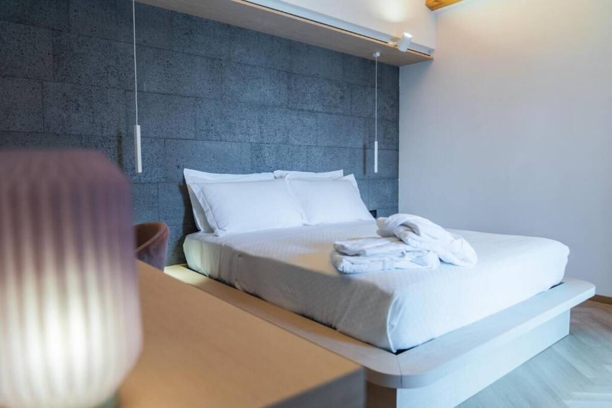 A modern hotel room with a bed, bedside table, and a textured wall.