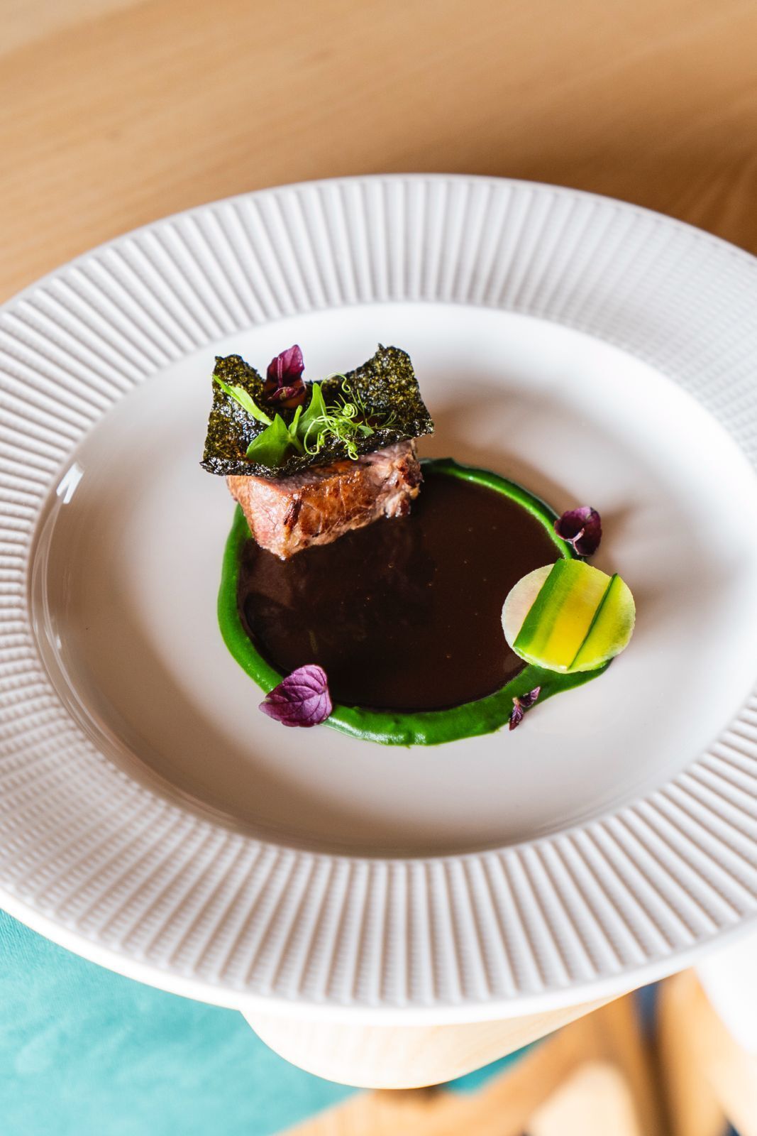 A white plate with a piece of meat, green sauce, and a dark liquid.