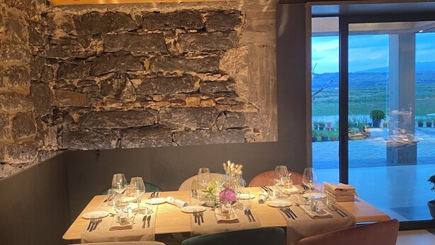 A dining area with a stone wall, wooden ceiling, and a view of a landscape through large windows. - Bahal dell Etna (Ramacca)