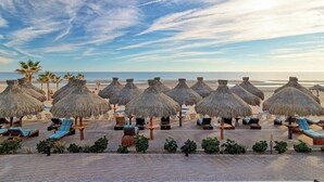 Ein Strandresort mit Reetdachschirmen und Liegestühlen, einem gepflasterten Weg und Blick auf das Meer.