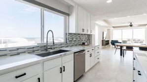 A modern kitchen with white cabinets, a stainless steel sink, and a large window overlooking a cityscape. - Brand New and Spacious 4 Bedroom CondoC-30202 (Puerto Peñasco)