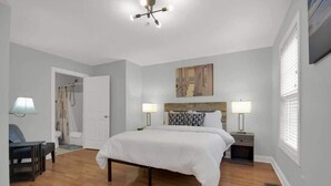 A bedroom with a bed, two bedside tables with lamps, a chair, and a door leading to a bathroom. - Lakefront Beautiful Townhome w/ Stunning Views! (North Charleston)