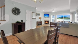 A dining area with a wooden table and chairs, a clock on the wall, a fireplace, and a view of the outdoors. - Lakefront Beautiful Townhome w/ Stunning Views! (North Charleston)