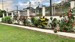 Área residencial murada com parede branca, plantas floridas e um poste de luz.