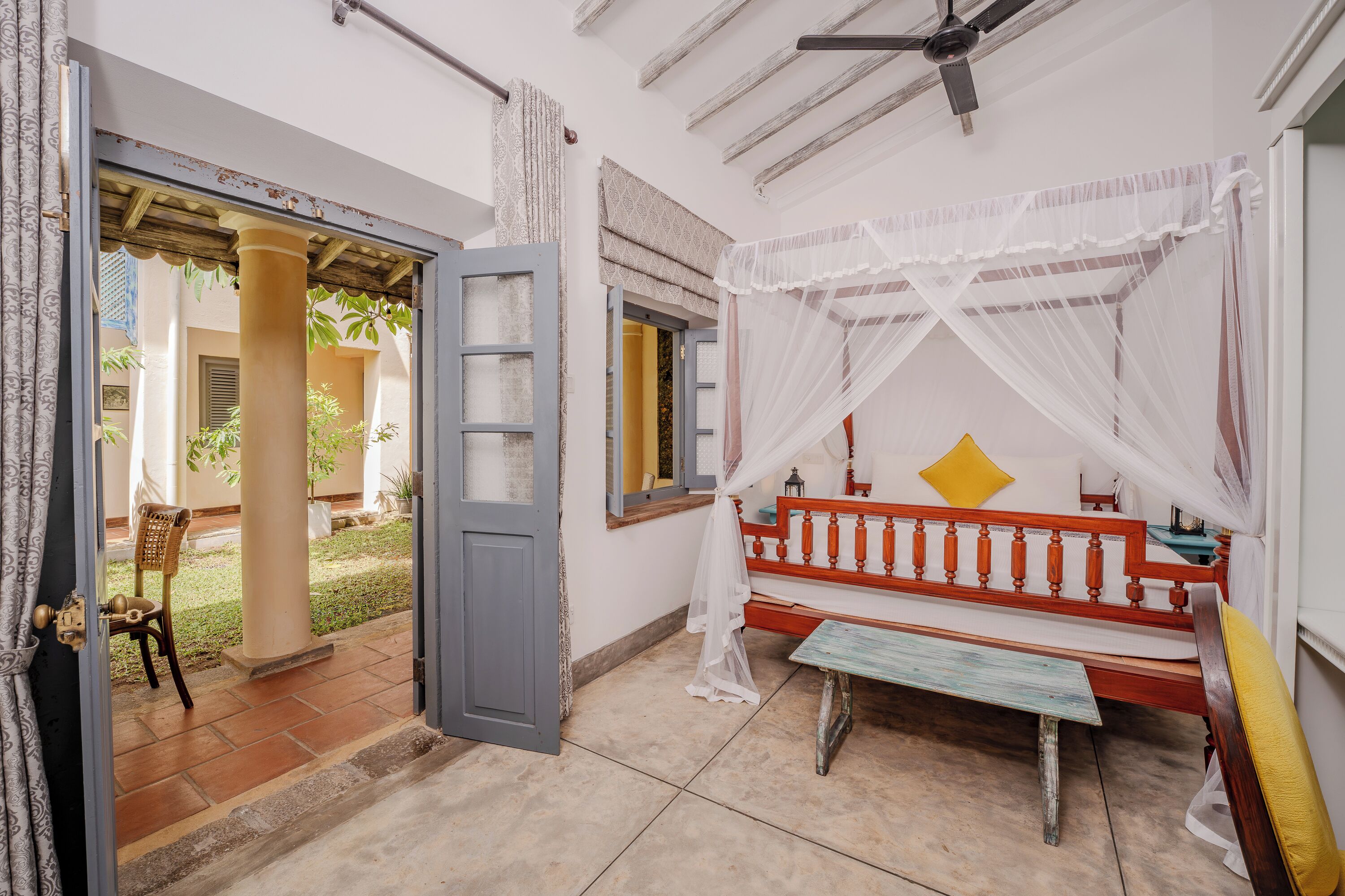 A room with a bed, a bench, a chair, a window, and a door leading to a balcony.