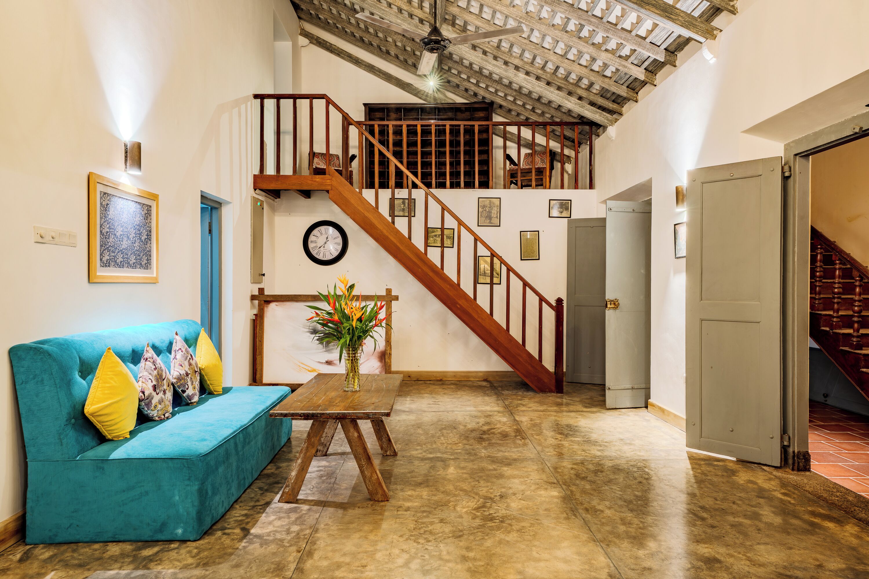 A spacious living area with a teal sofa, a wooden table with a vase, and a staircase leading to an upper level.