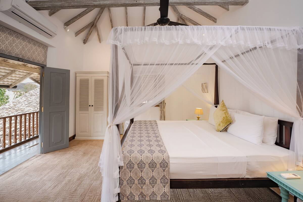 A bedroom with a canopy bed, a patterned bedspread, a bedside table, and a nightstand.