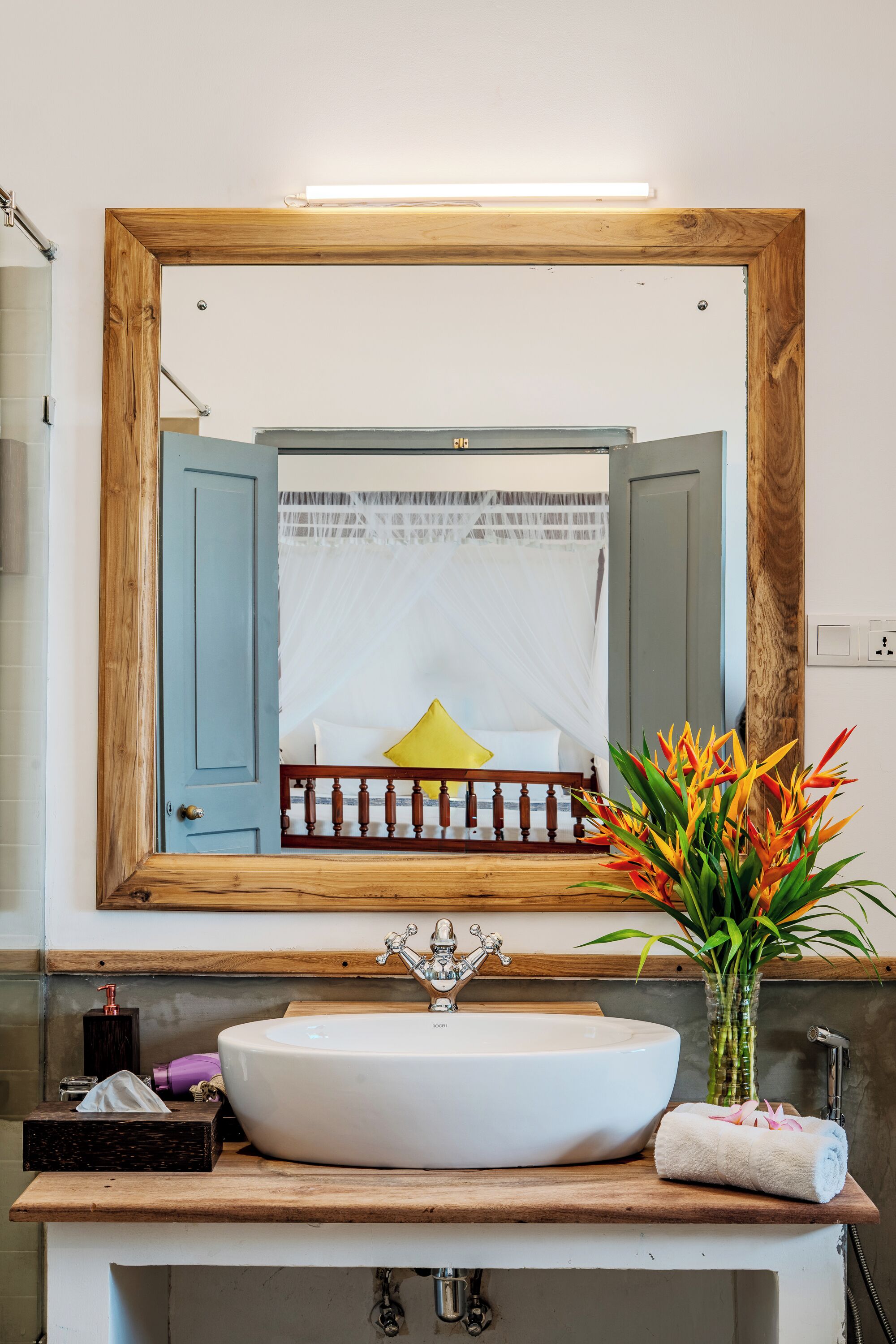 Ein Badezimmer mit einem spiegelnden Holzbettrahmen, einem weißen Waschbecken und einer Blumenvase.