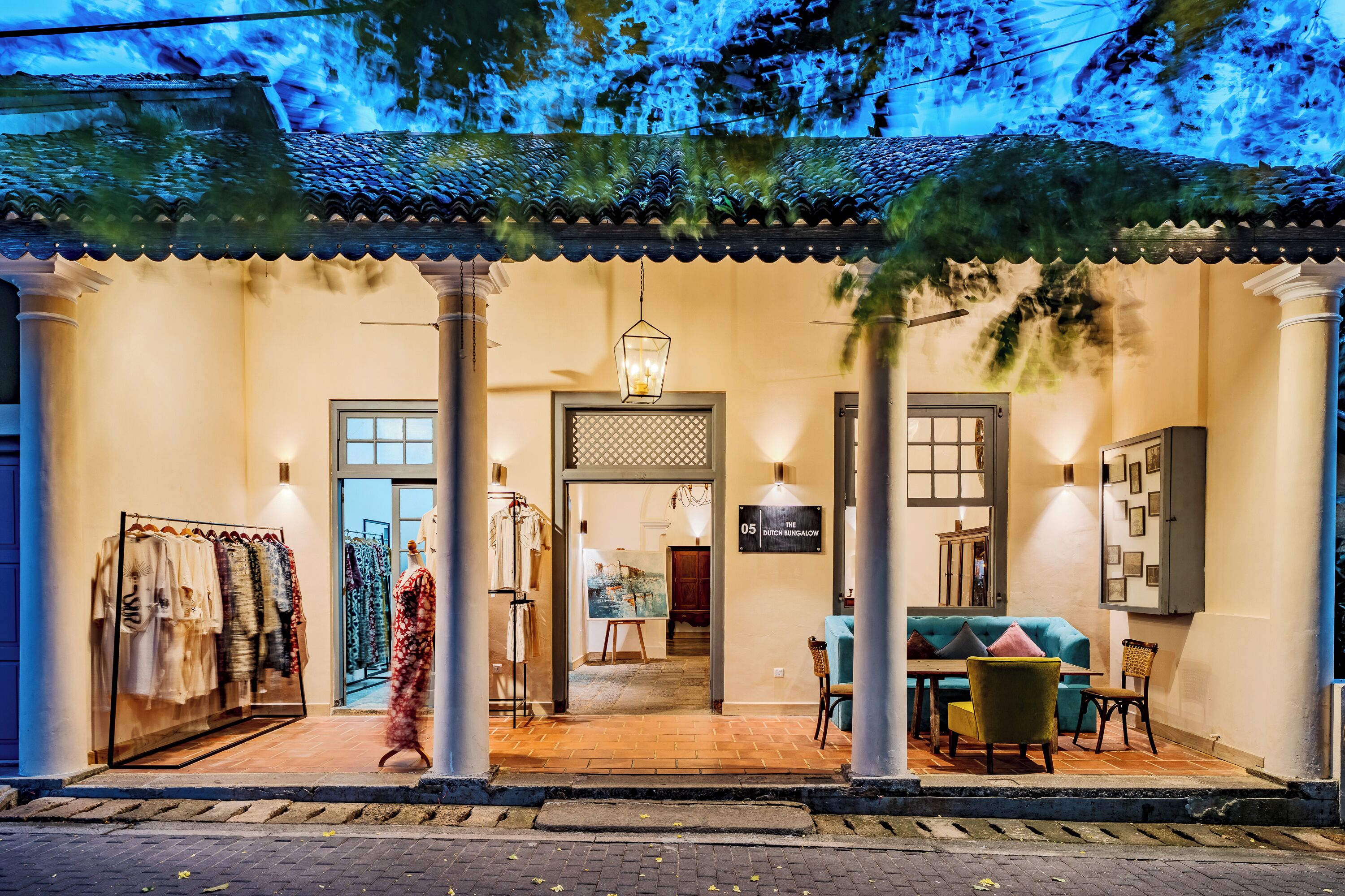 A traditional building with a tiled roof, a clothing store on the left, and a dining area with a table and chairs in the center.