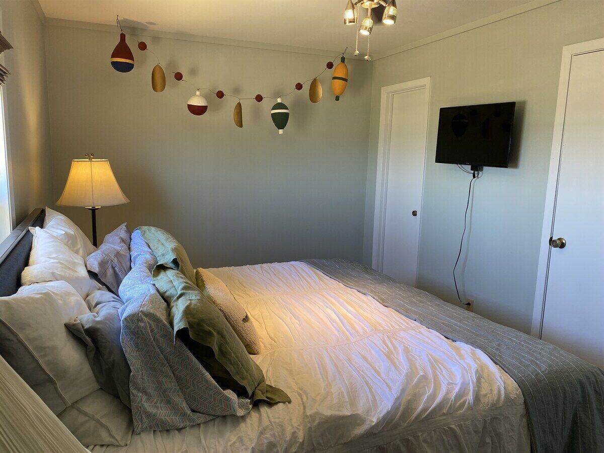 A bedroom with a bed, pillows, a lamp, a television, and a wall decoration.