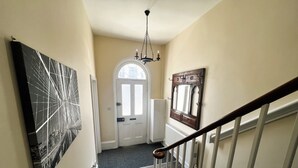 Una escalera con barandilla, una puerta con panel de vidrio esmerilado y un candelabro.