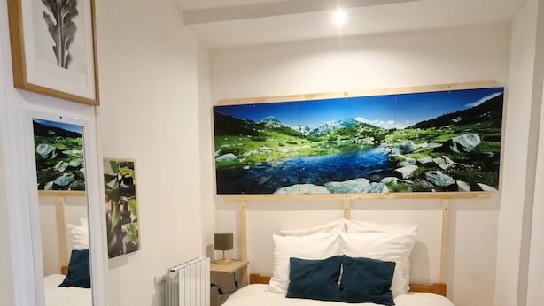 Ein Schlafzimmer mit einem großen Bett, einem Holzkopfstück, einem Nachttisch und einem Beistelltisch, sowie einem großen gerahmten Landschaftsbild über dem Bett.