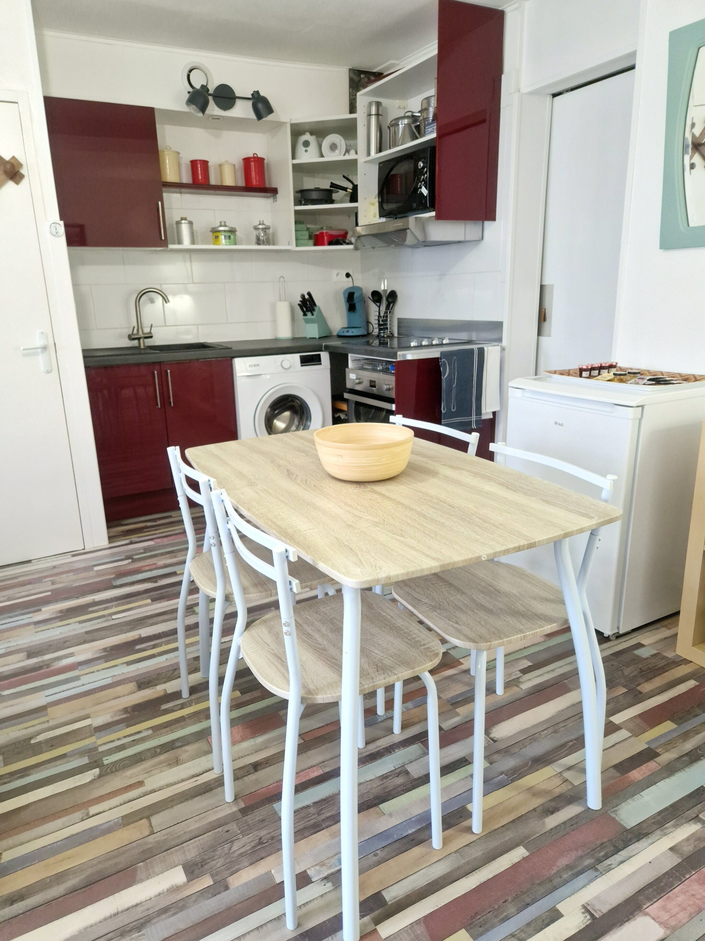 Une cuisine compacte avec une table en bois, des chaises blanches, un lave-linge et un four à micro-ondes.
