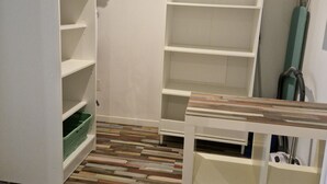 Ein begehbarer Kleiderschrank mit offenen Regalen, Holzboden und einem Staubsauger in der Ecke.