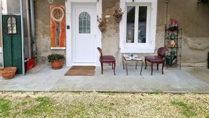 Eine überdachte Terrasse mit zwei Holzstühlen, einem kleinen Tisch, einem Blumentopf und einer Tür mit dem Schild "THE WALSH".