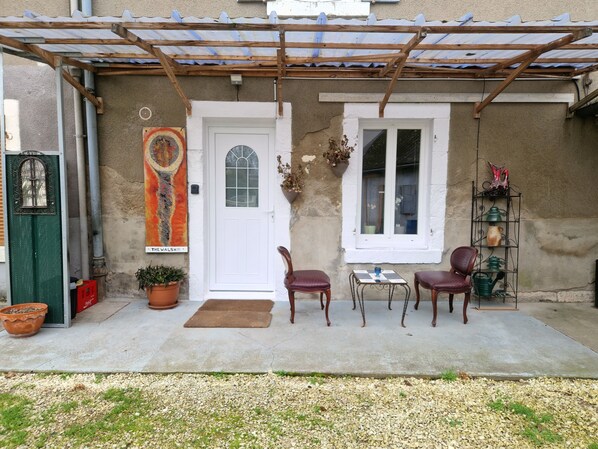 A covered patio with two wooden chairs, a small table, a potted plant, and a door with a sign reading "THE WALSH". - The Walsh Bien Rare, Calme Dans une Cour Privé Sans Passage ni vi à vi (Bourges)