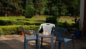 A patio area with two plastic chairs, a table, and potted plants. - The Raghav - Villa/Farmhouse Getaway amidst Nature (Gurugram)