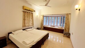 A hotel room with a bed, a window with curtains, a ceiling fan, and a wall-mounted air conditioner. - The Raghav - Villa/Farmhouse Getaway amidst Nature (Gurugram)