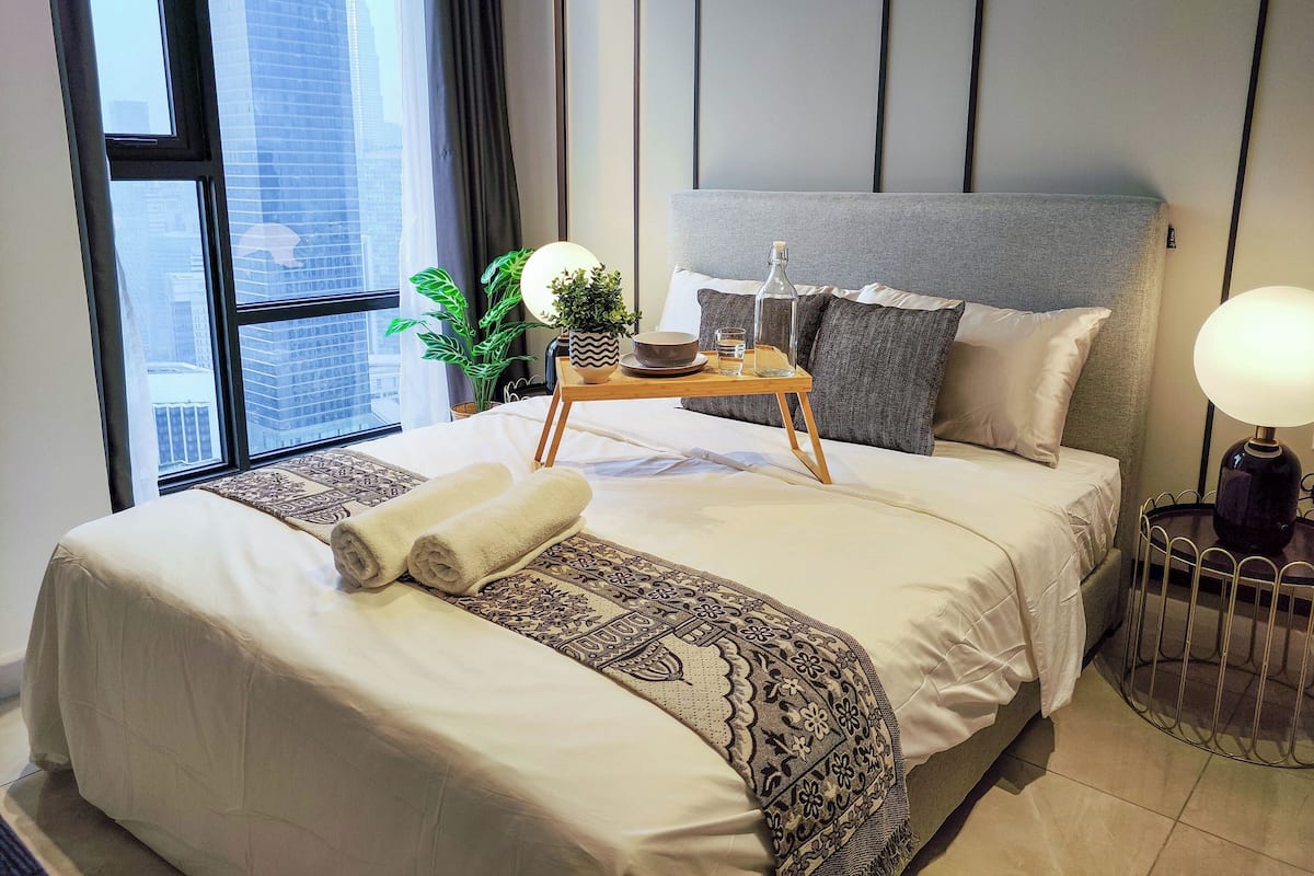 Un hotel moderno con una cama grande, una mesita de noche con lámpara, una planta en maceta y vistas a la ciudad.