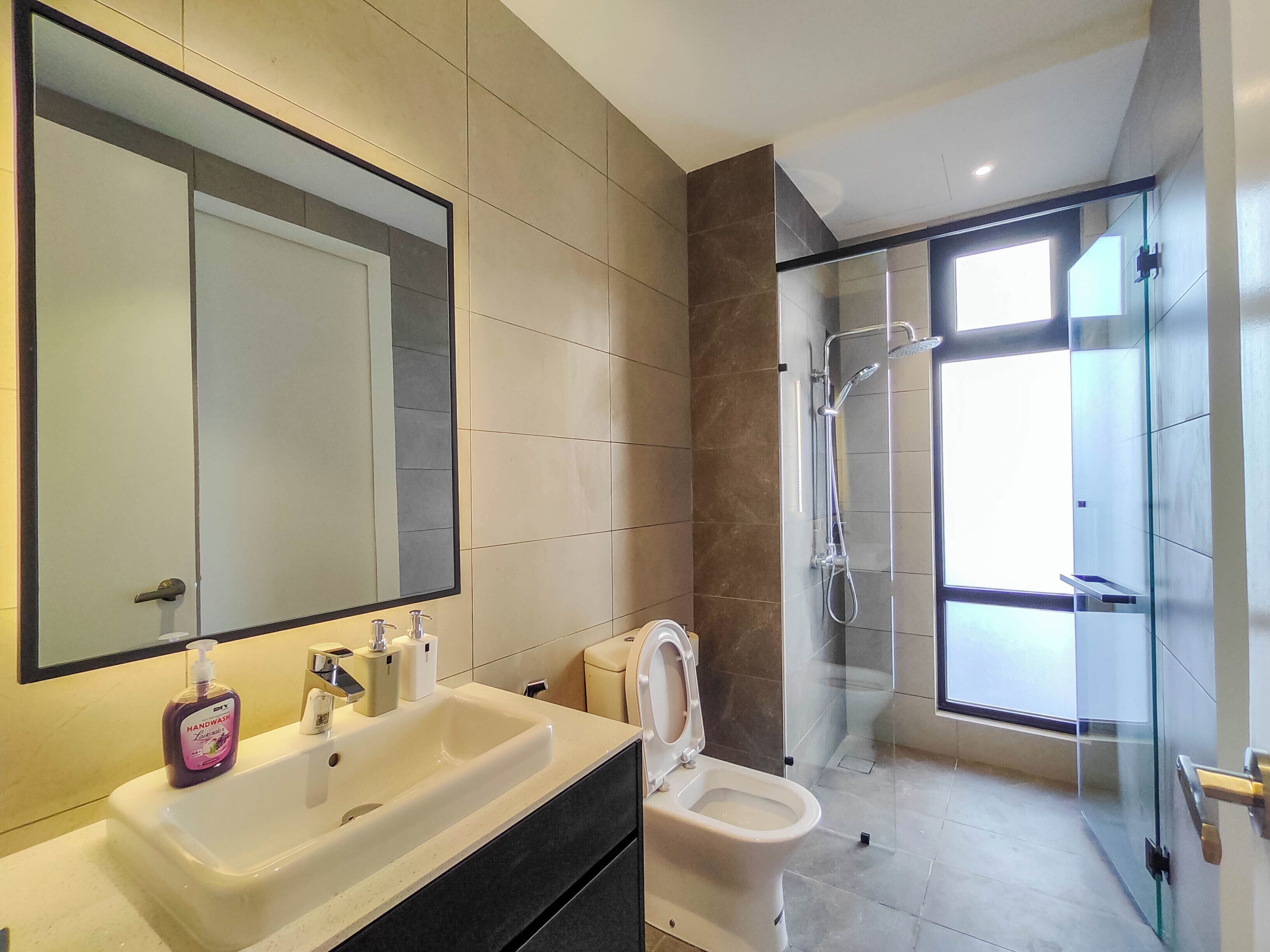 Un baño moderno con un espejo grande, un lavamanos, un inodoro y una zona de ducha con mampara de vidrio.
