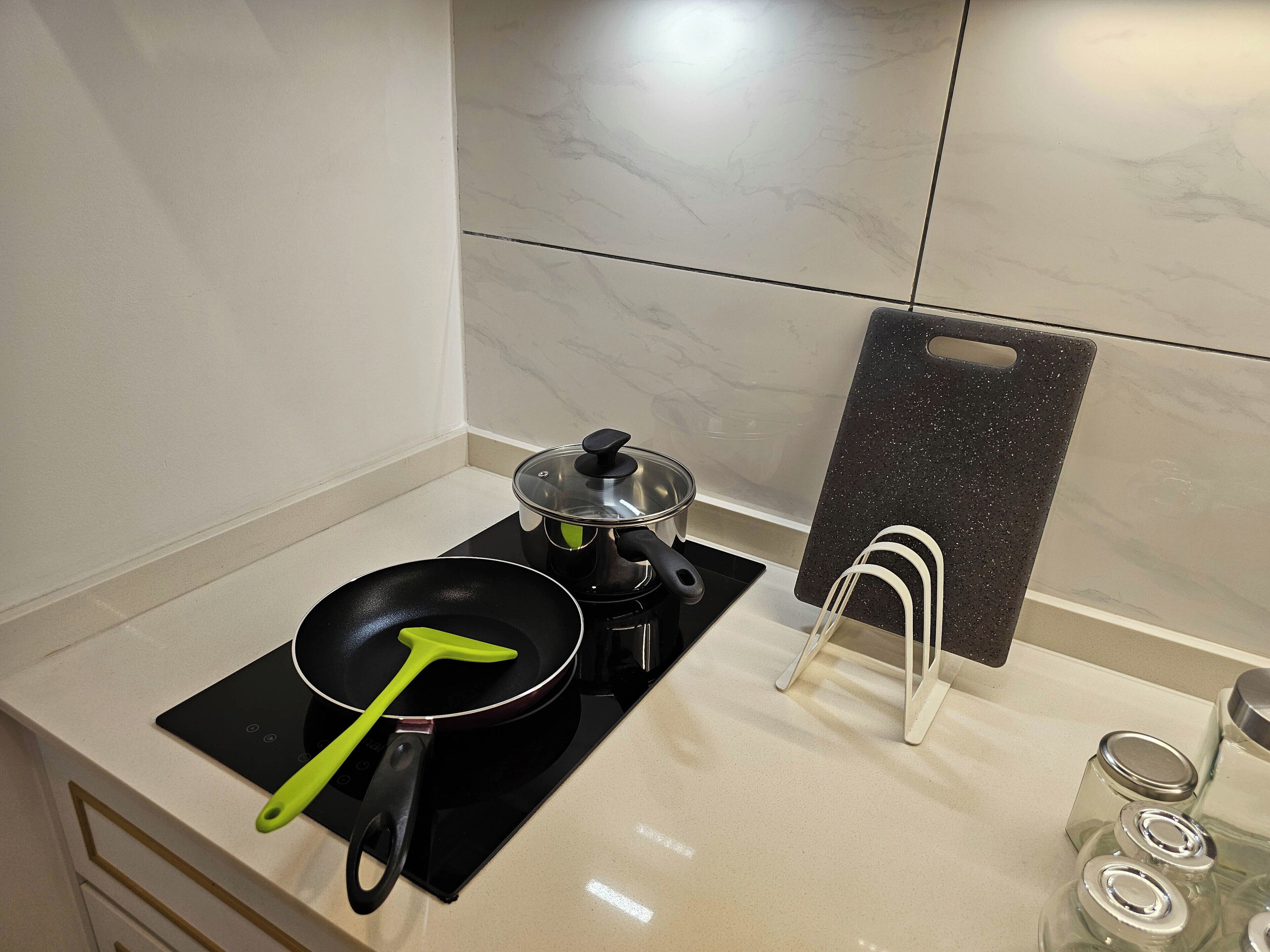 A kitchen with a stove, a frying pan, a pot, and a spice rack.