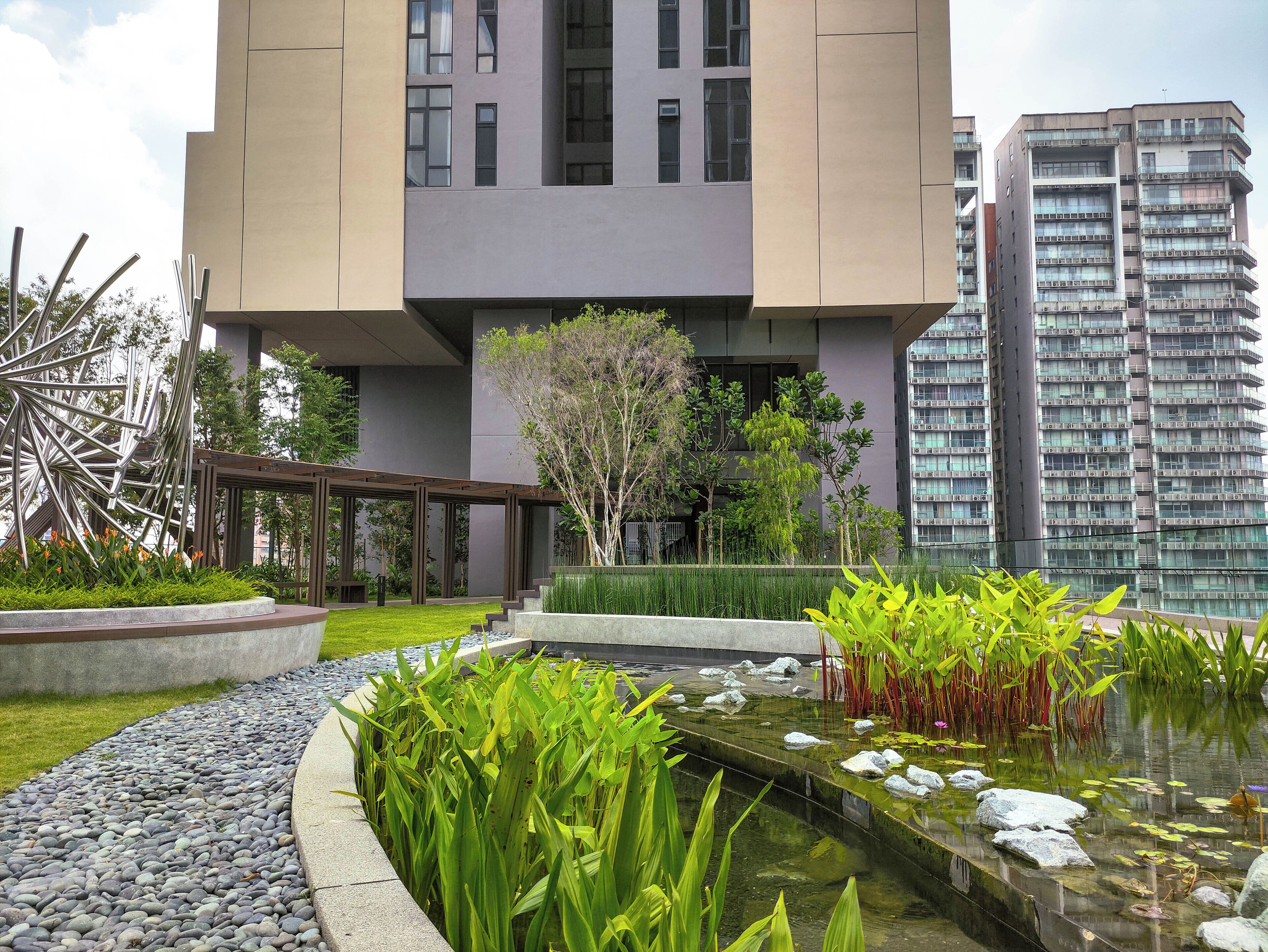 A modern building with a courtyard featuring a water feature, greenery, and a metal sculpture.