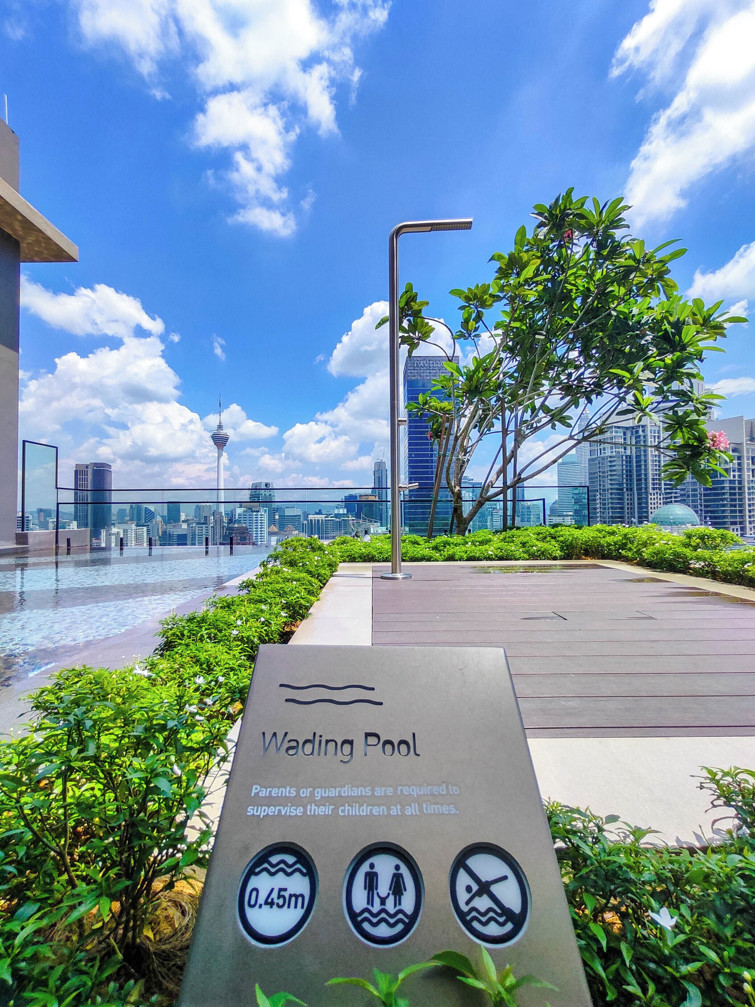 A sign for the Wading Pool with safety instructions, surrounded by greenery and a cityscape in the background.