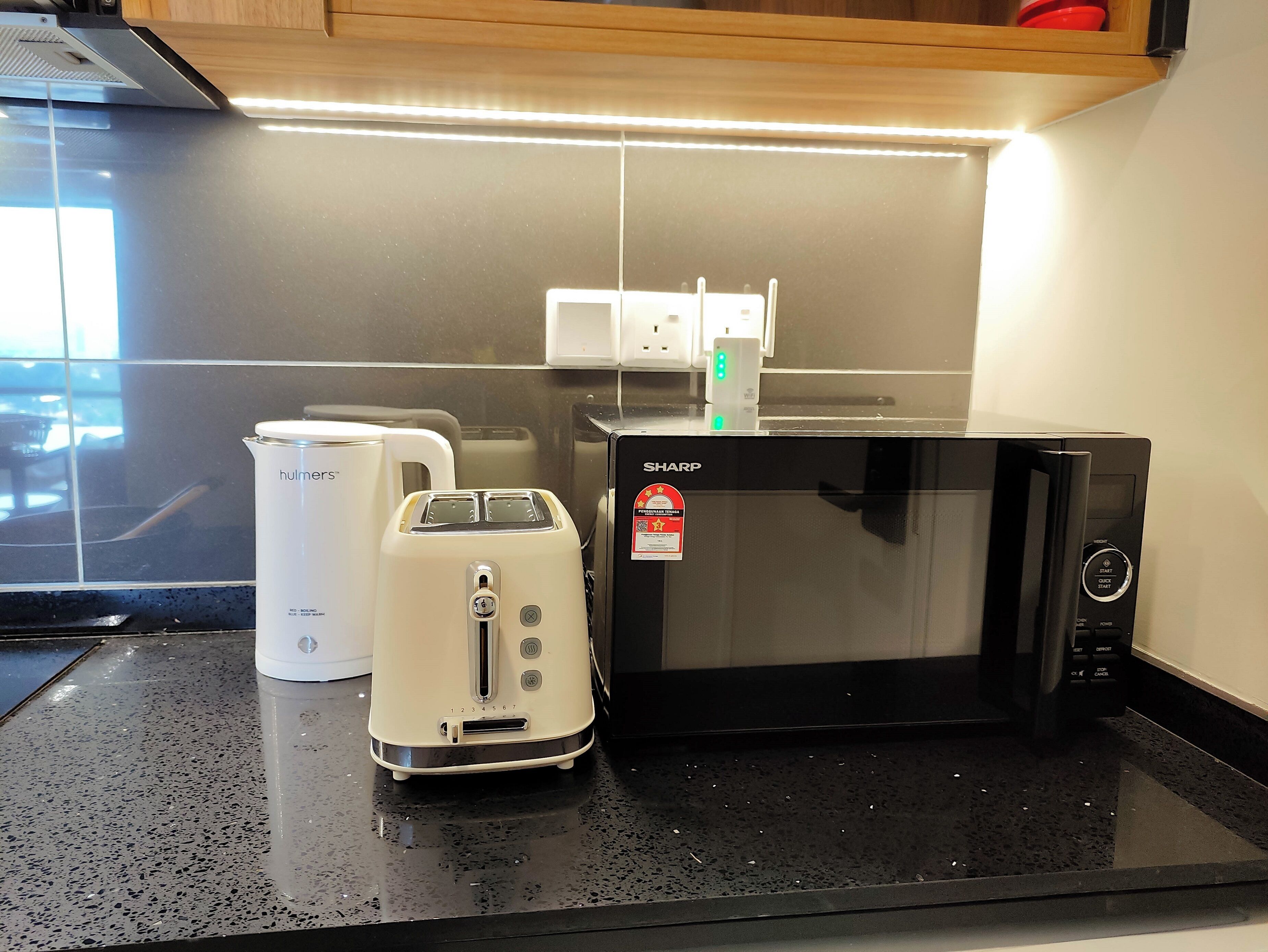 A kitchen with a black countertop, a white toaster, a white electric kettle, and a black microwave.