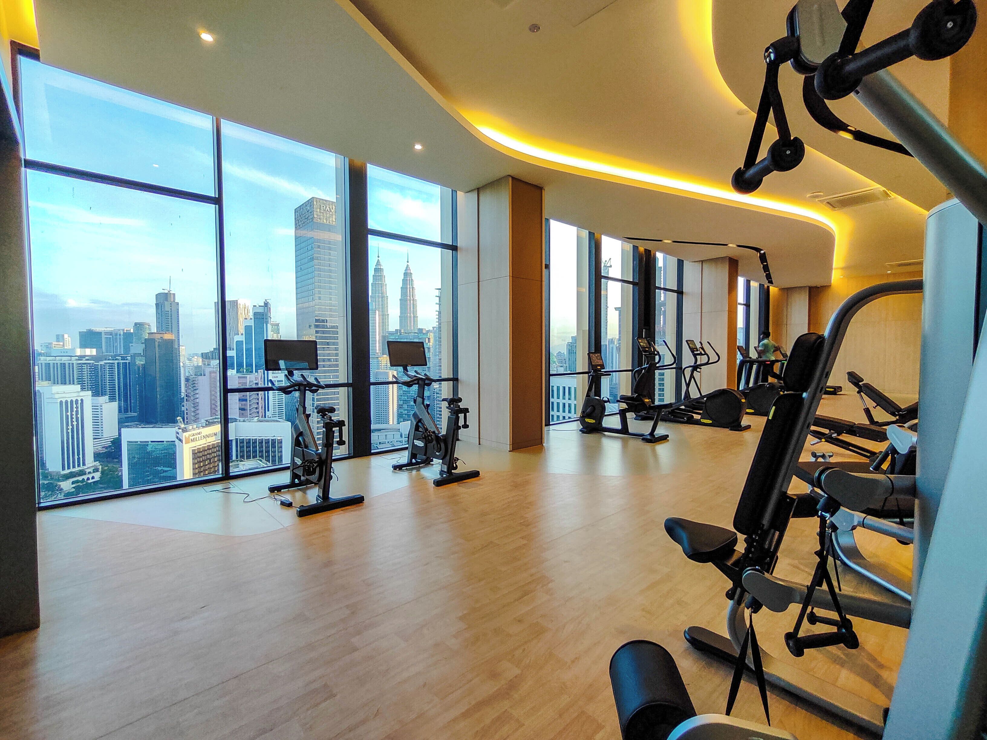 A gym with large windows offering a city view, various exercise equipment, and a wooden floor.