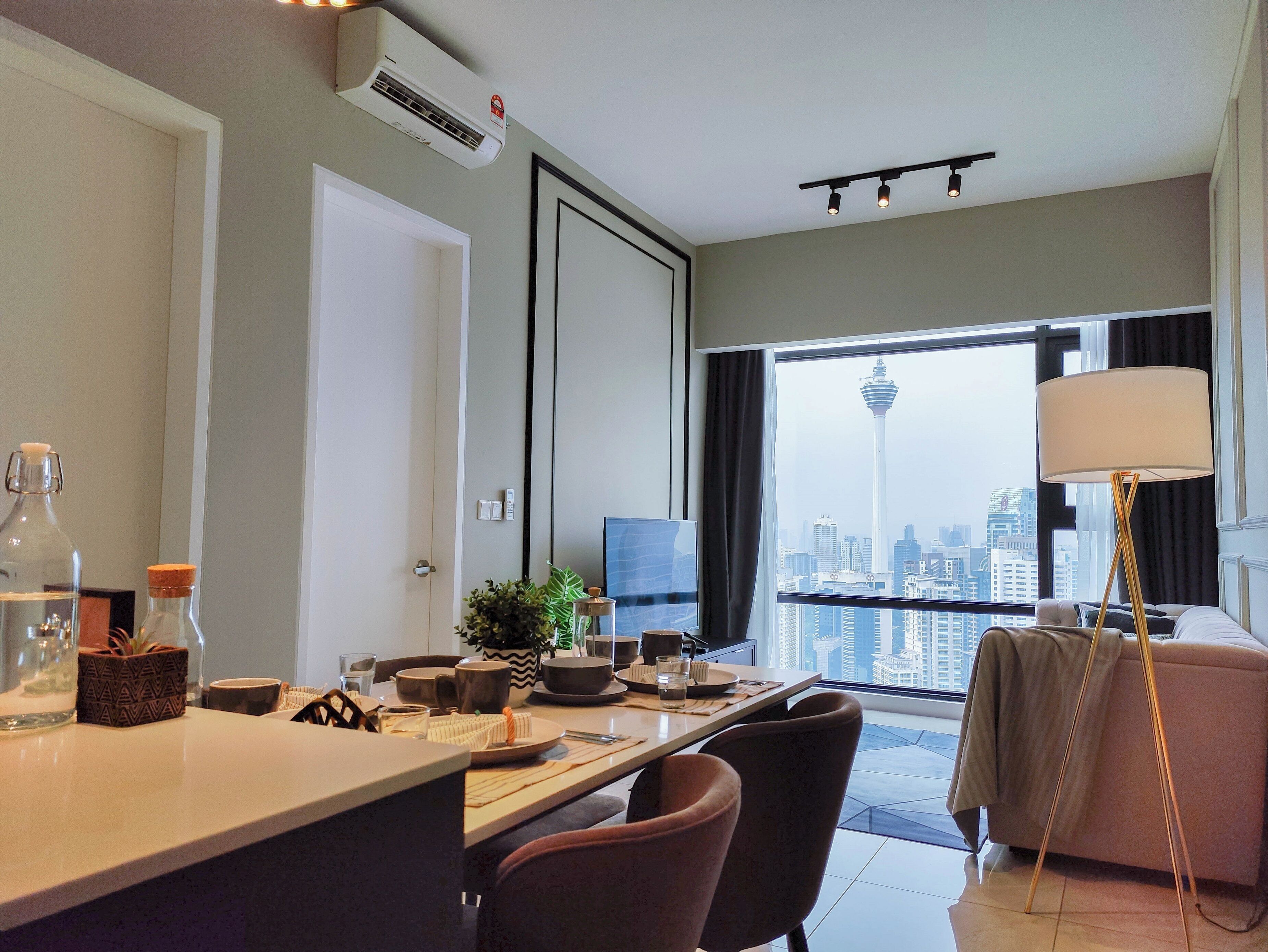 Habitación de hotel moderna con comedor, un amplio ventanal con vista a la ciudad, escritorio con computadora y sofá.