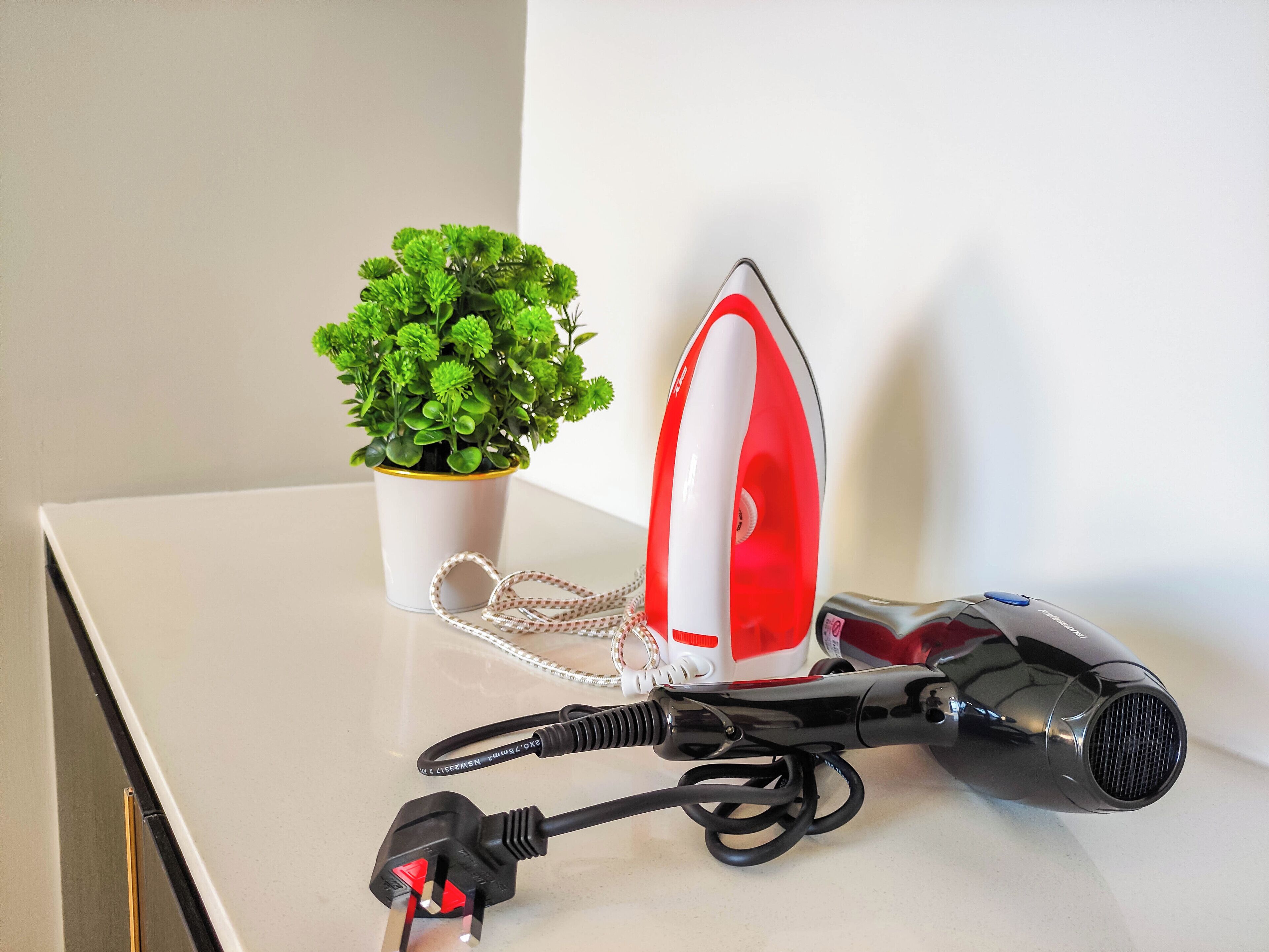 A table with an iron, a hairdryer, and a potted plant.