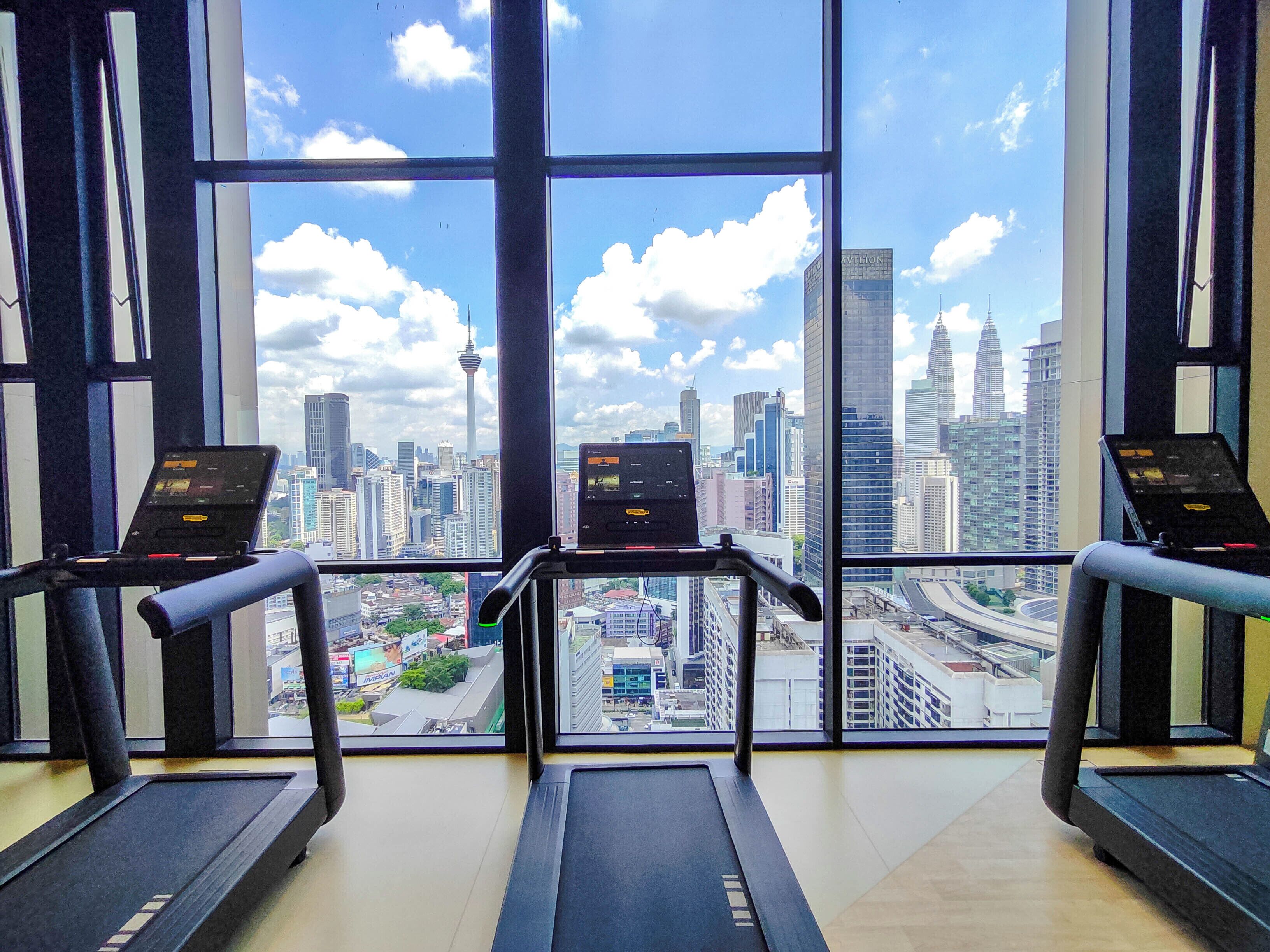 A gym with treadmills and exercise equipment, large windows with a city view.