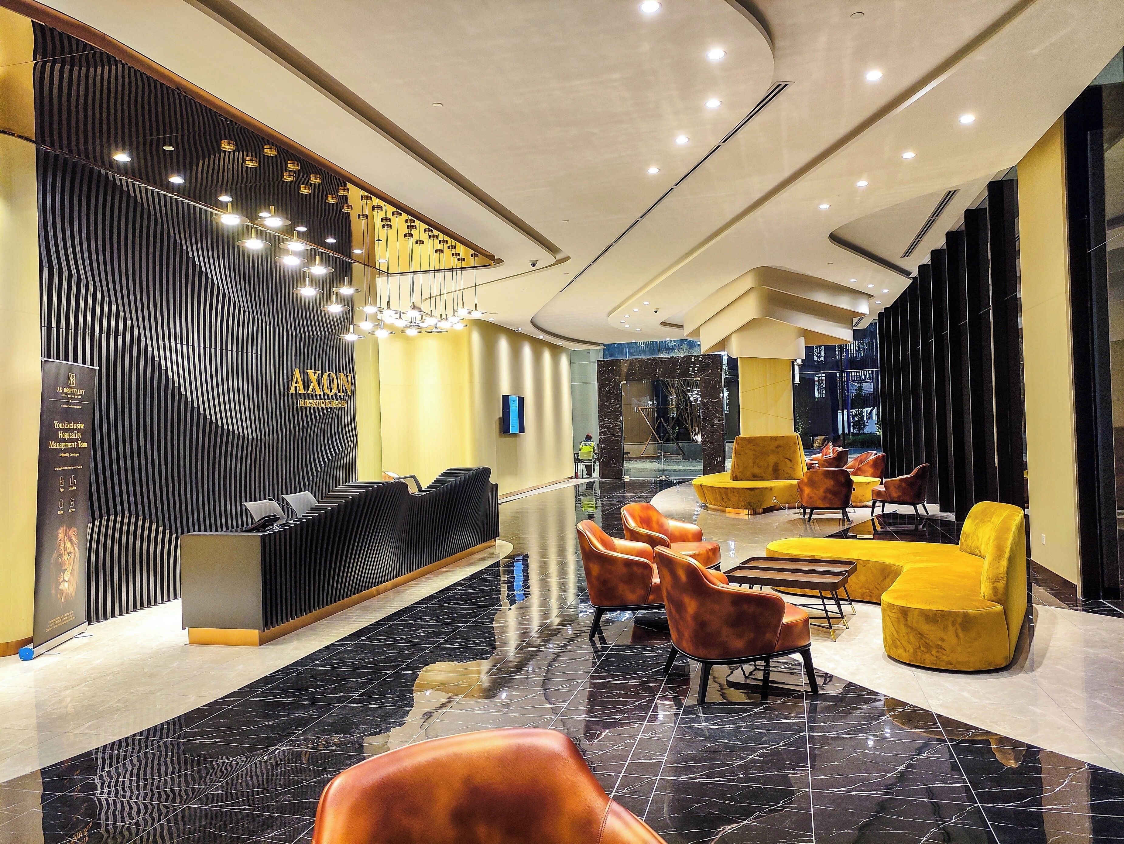 A modern hotel lobby with a reception desk, seating area, and a large mirror.
