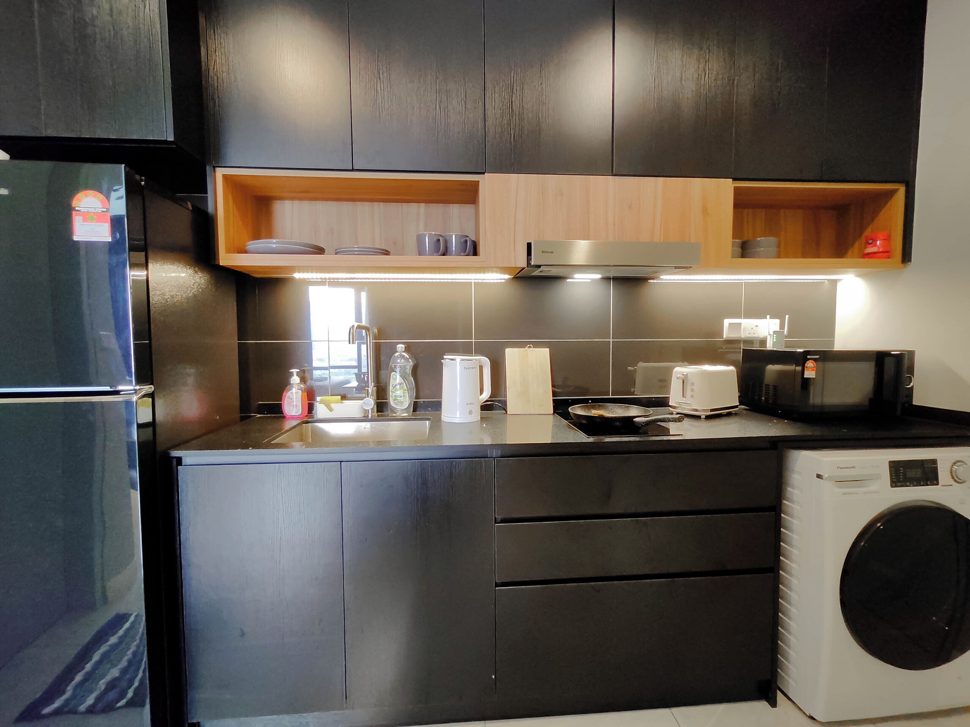 A modern kitchen with dark cabinets, a built-in microwave, a toaster, and a washing machine.