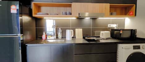 Una cocina moderna con armarios oscuros, un microondas integrado, un tostador y una lavadora.