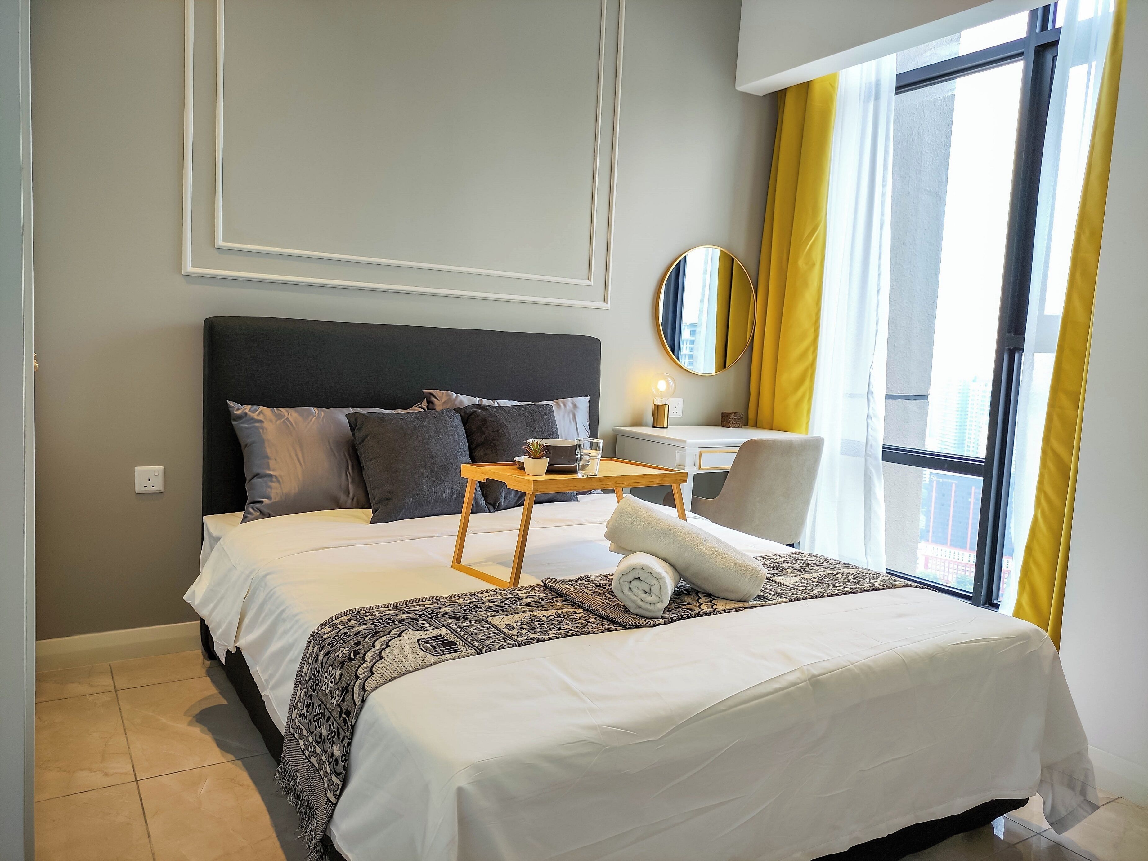 A hotel room with a large bed, a bedside table with a lamp, a chair, and a window with curtains.