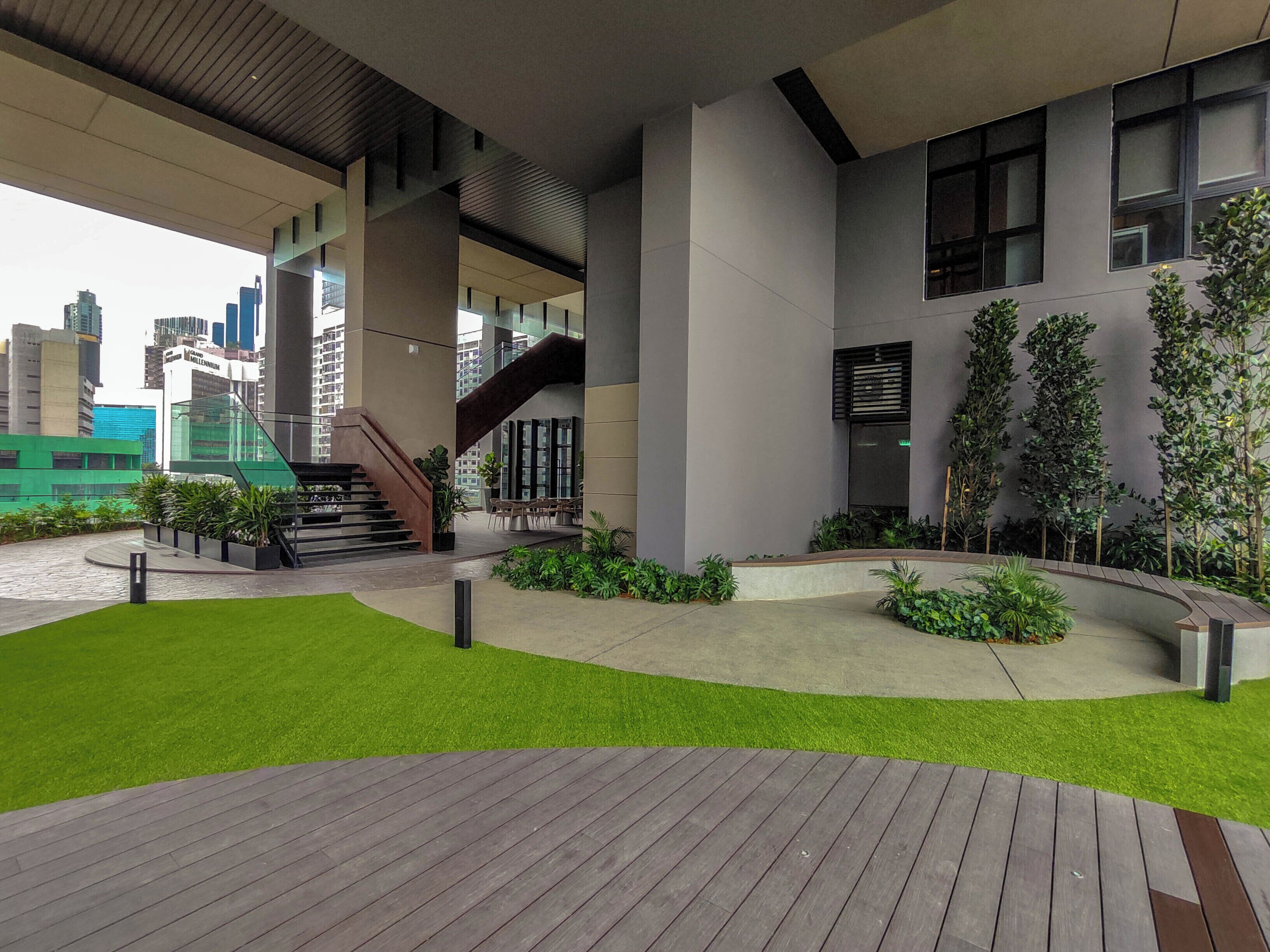 A modern building with a wooden deck, green lawn, and a staircase leading to an upper level.