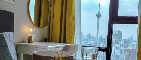 A hotel room with a bed, a bedside table with a lamp, a window with a city view, and a view of a tower.