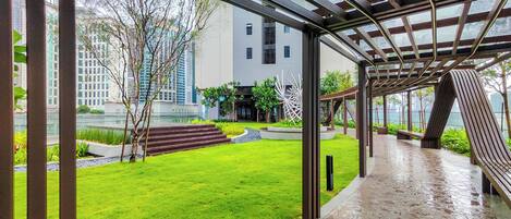 A covered outdoor area with a glass roof, a well-maintained lawn, and a building in the background.
