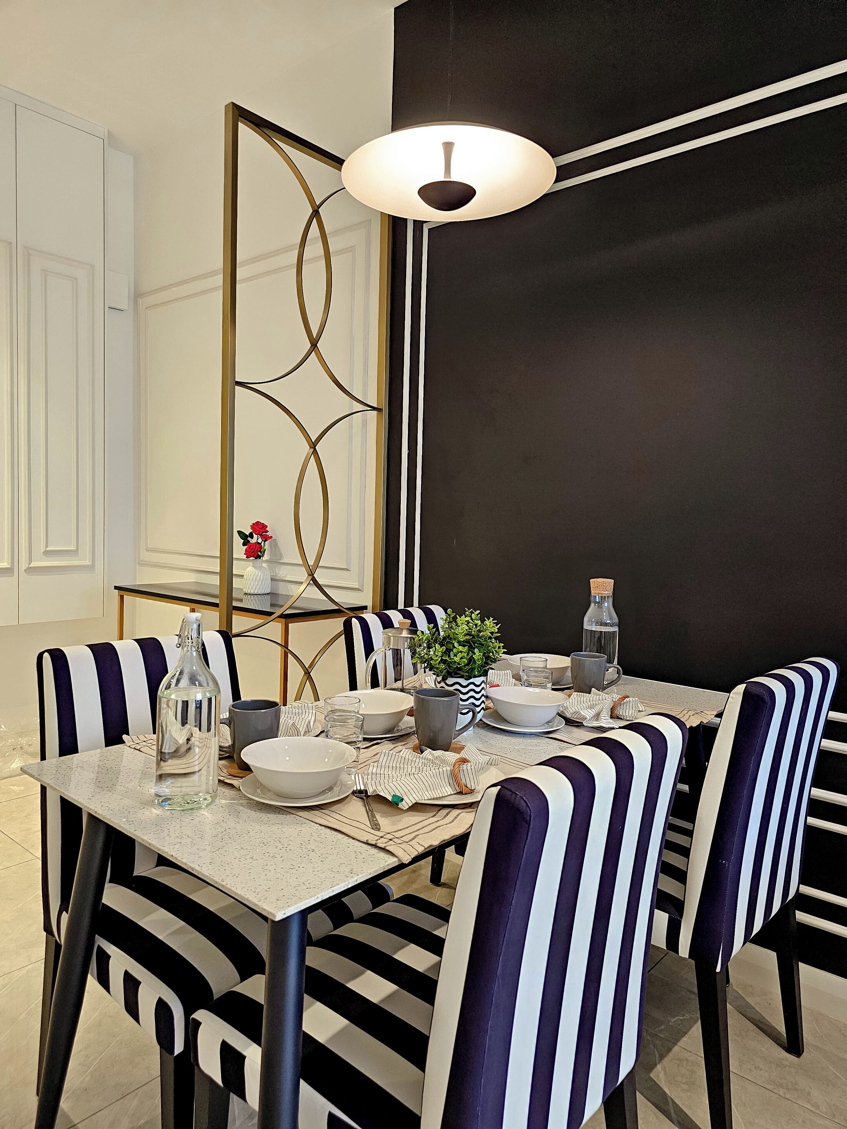 Un comedor con sillas a rayas, una mesa servida con platos, tazones y una botella.