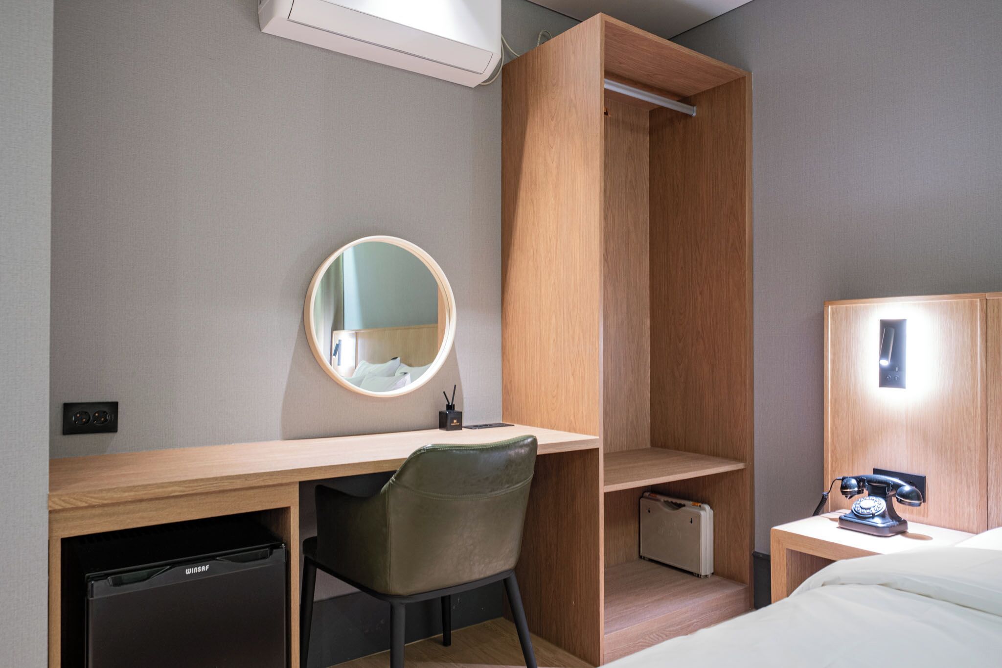 Ein kleines Hotelzimmer mit Schreibtisch, Stuhl, Bett, Kleiderschrank und einer kleinen Küchenzeile.