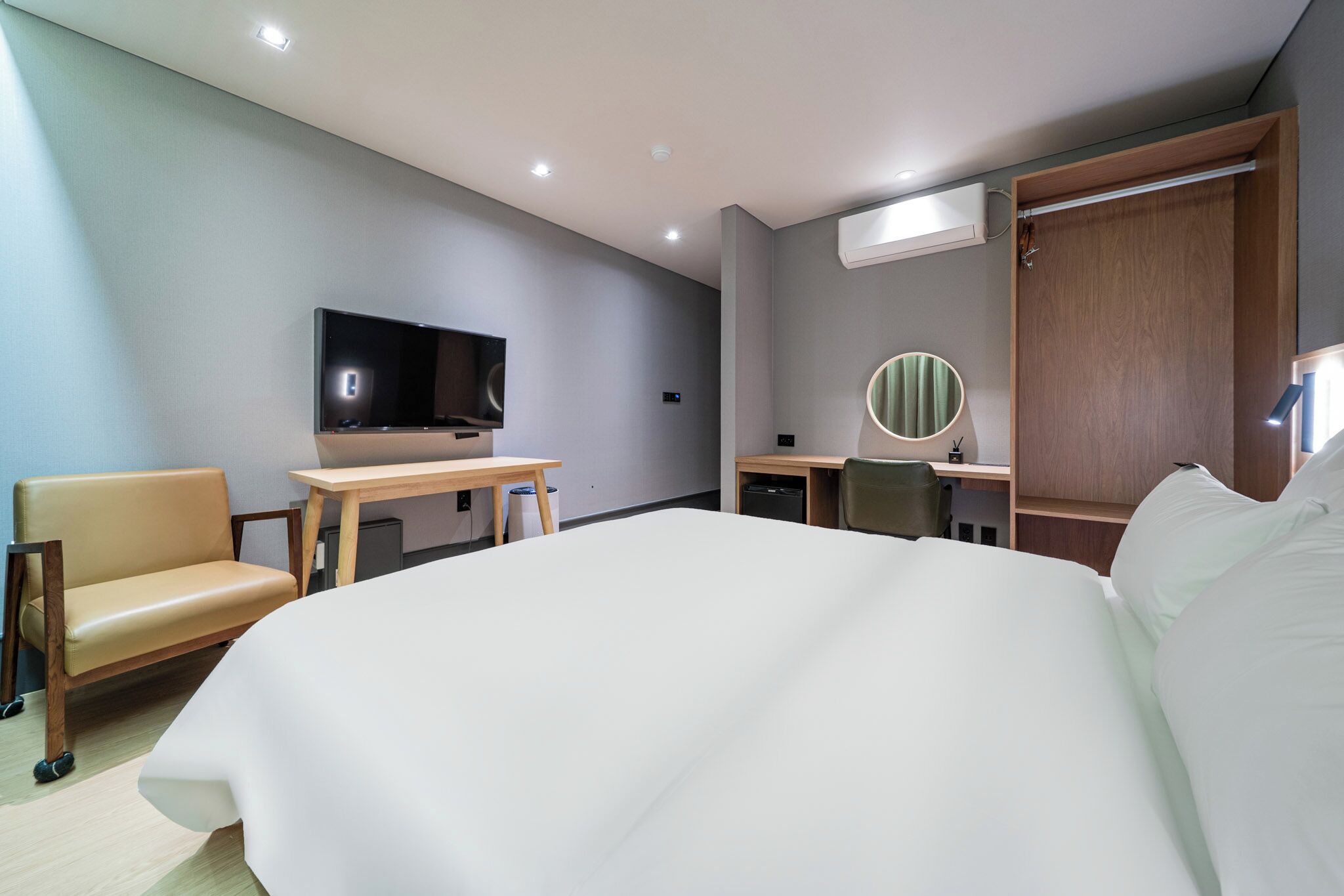 A modern hotel room with a large bed, a desk, a chair, a television, and a mirror.