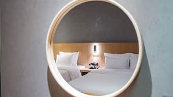 A hotel room with a large oval mirror reflecting a bed, a nightstand with a telephone, and a wall-mounted light.