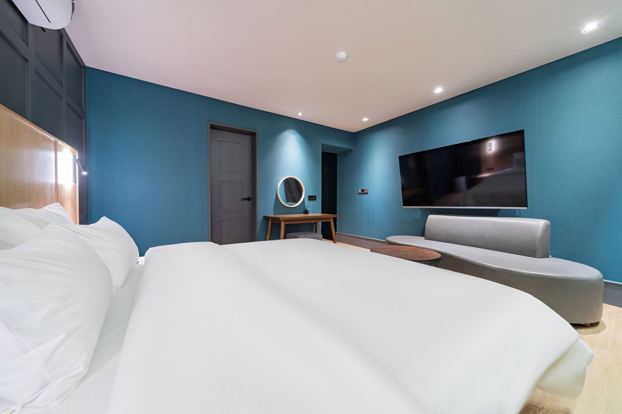 Una habitación de hotel moderna con una cama grande, una zona de estar, un televisor y una mesita con un espejo.