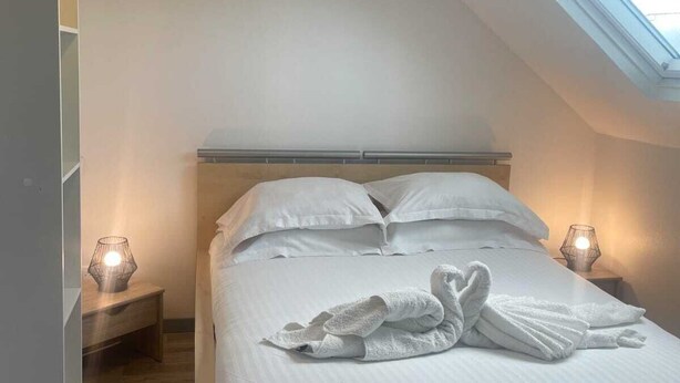 Ein Schlafzimmer mit Dachfenster, einem Bett mit weißen Leinentüchern, zwei Nachttischlampen und einem Holznachttisch.