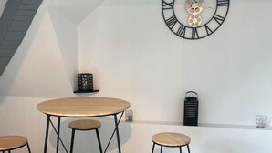 Ein Loft-Zimmer mit Holzboden, einem runden Tisch mit Hocker, einer Wanduhr und einem kleinen Regal mit Dekoration.