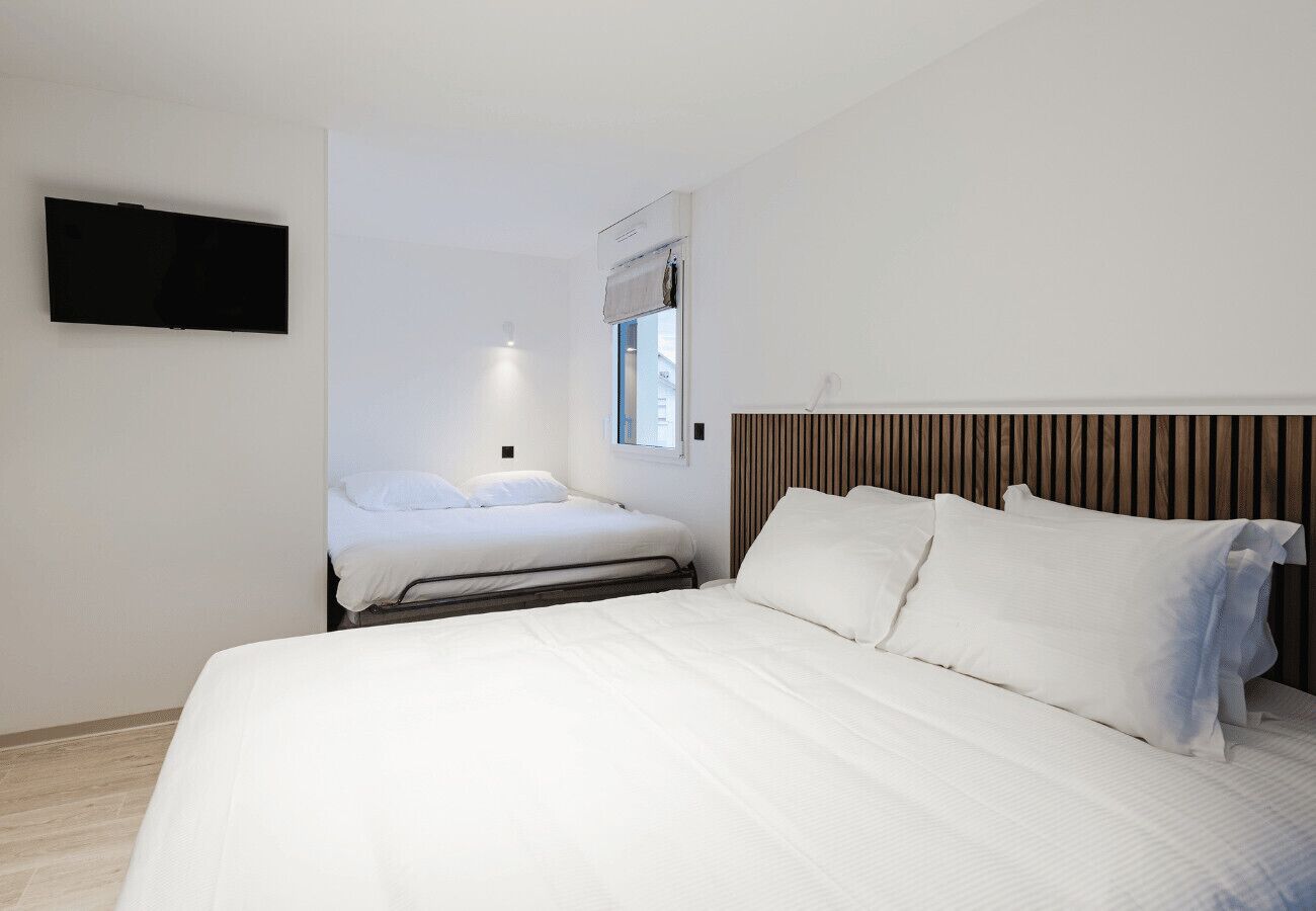 Ein modernes Schlafzimmer mit einem großen Bett, einem kleineren Bett, einem flachbildfernseher an der Wand und einem Fenster mit Ausblick.