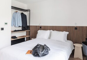 Ein Hotelzimmer mit einem Bett, einem Kleiderschrank mit Kleidung, einem Nachttisch mit Lampe und einem Sessel.