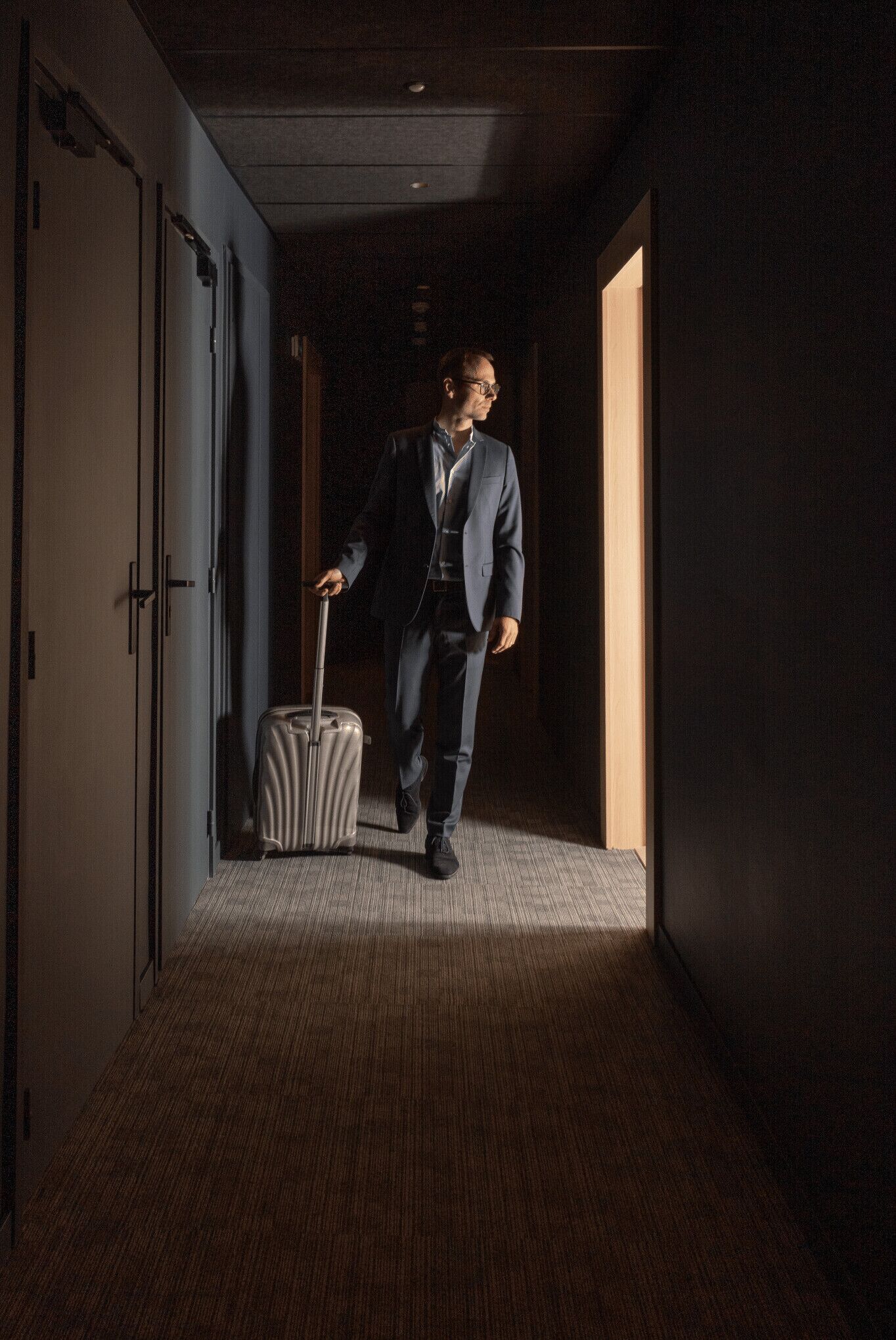 A man in a suit walking through a hotel corridor with a suitcase.