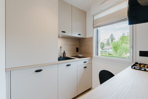 Eine moderne Küche mit weißen Schränken, einem Fenster mit Blick auf Grünflächen und einer kleinen Spüle mit einer Flasche und einer Küchenpapierrolle.